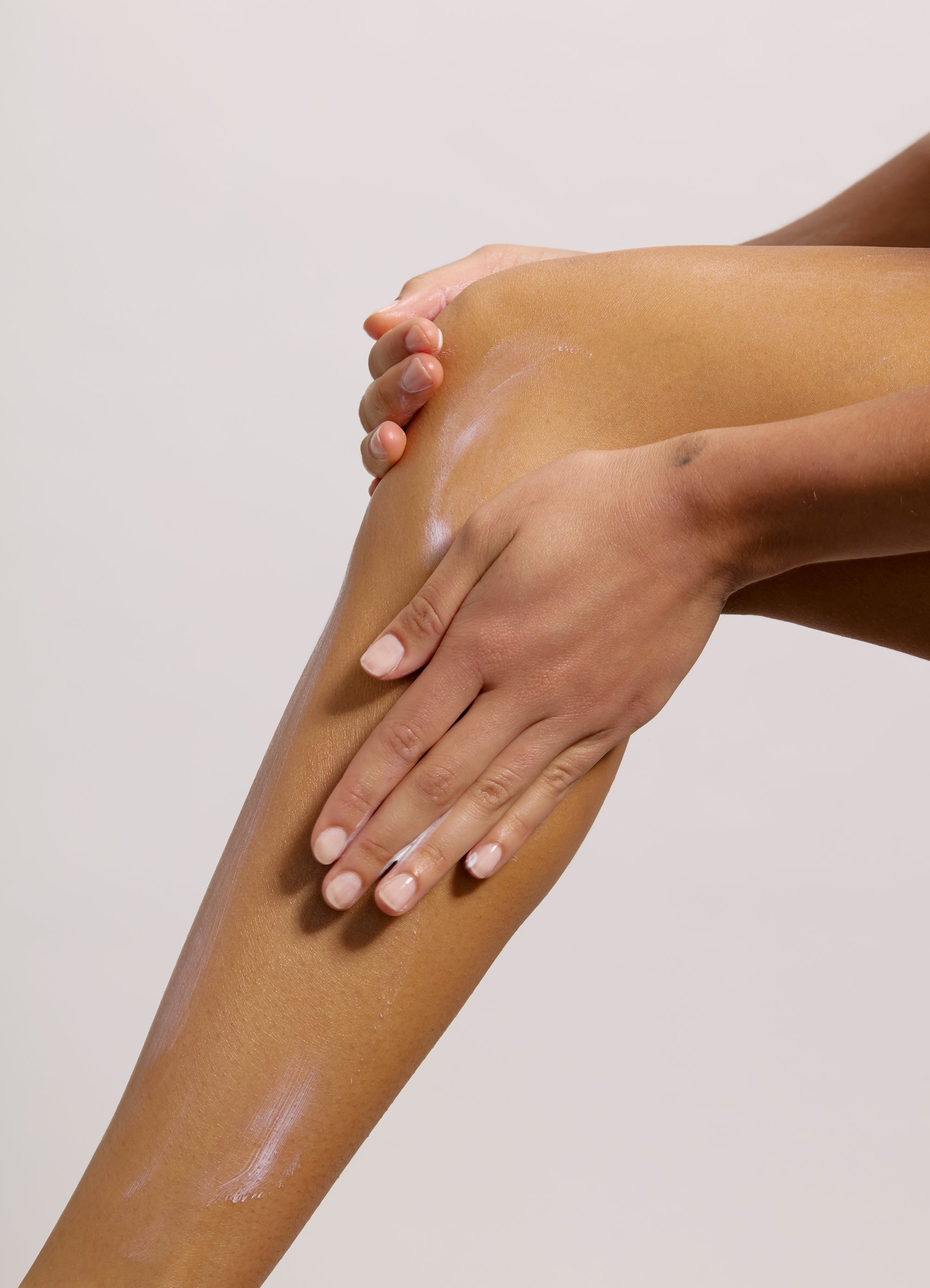 A person is applying Peak Performance SPF50 - SAMPLE from Freaks of Nature Skincare to their smooth, tan leg with both hands, focusing on the knee area. The background is plain and light-colored, highlighting the moisturized skin infused with red algae MAA extracts and the gentle action of self-care.