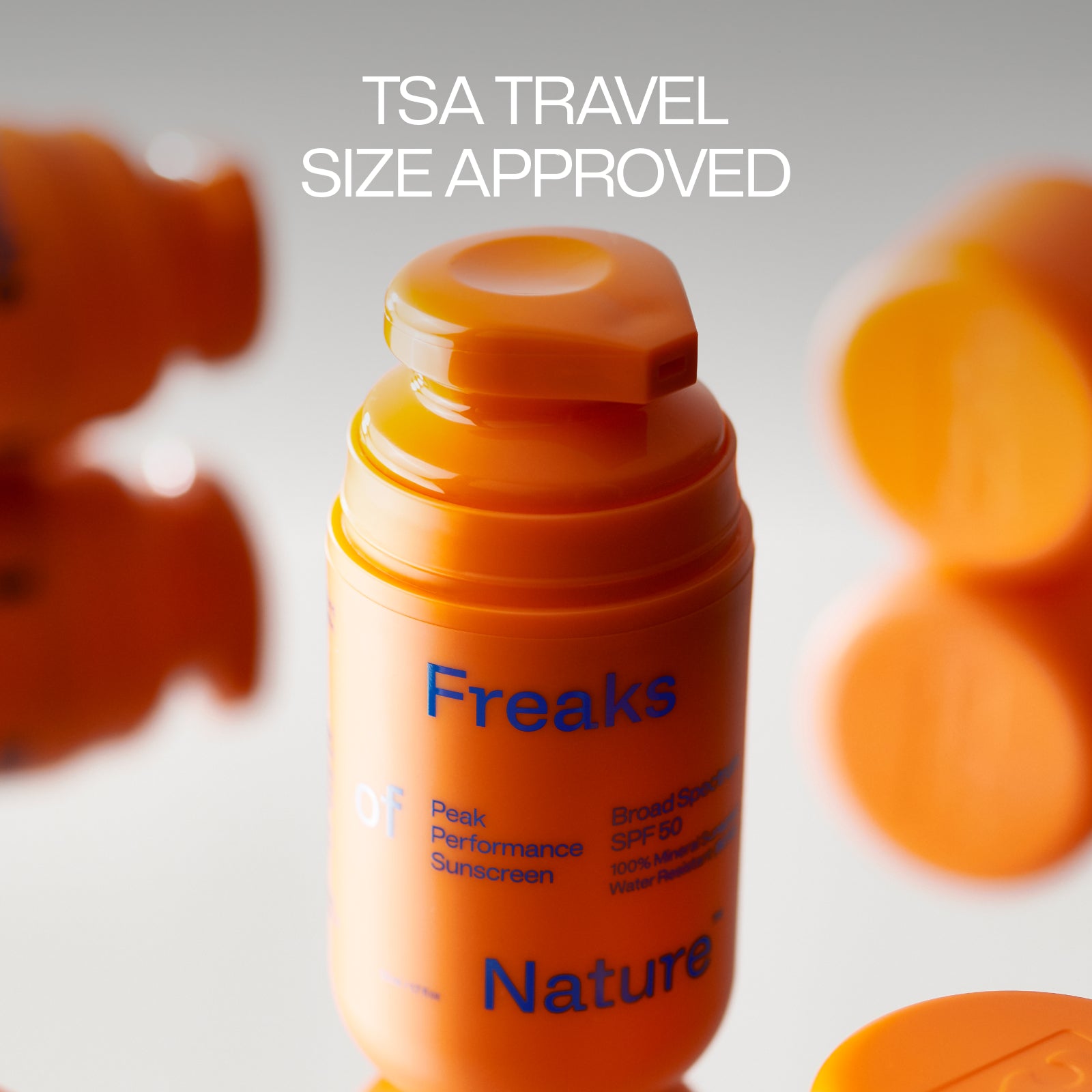 An orange bottle labeled "Peak Performance SPF50" by Freaks of Nature Skincare, TSA travel size approved, features Broad Spectrum SPF 50. With its vegan spider silk protein blend, it stands out vividly against the blurred backdrop of similar bottles, highlighting its unique formulation.