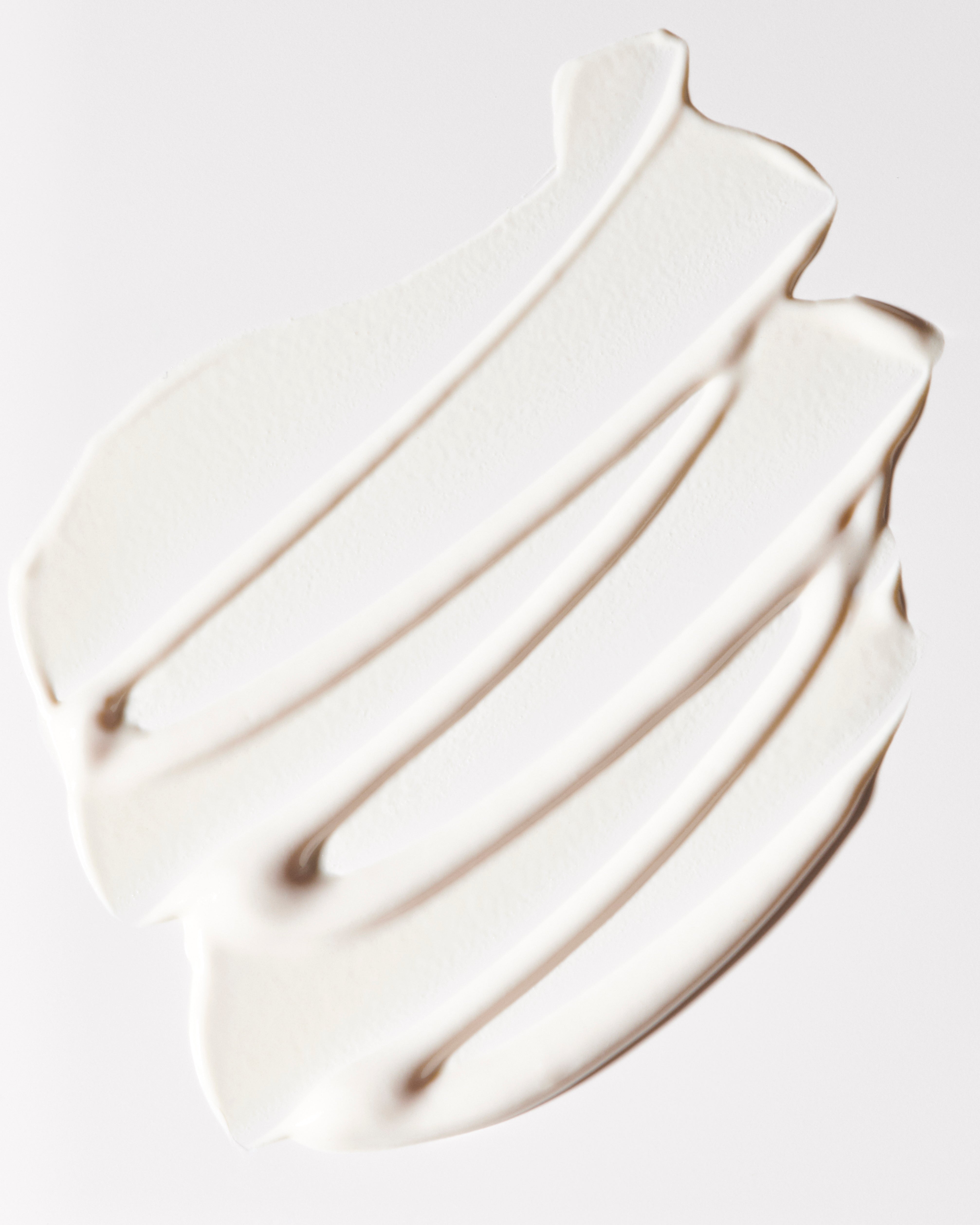 A close-up of Freaks of Nature Skincare's Daily System SPF 30 Sunscreen smeared on a smooth, white surface, forming an abstract pattern with four diagonal stripes. The texture appears soft and creamy.