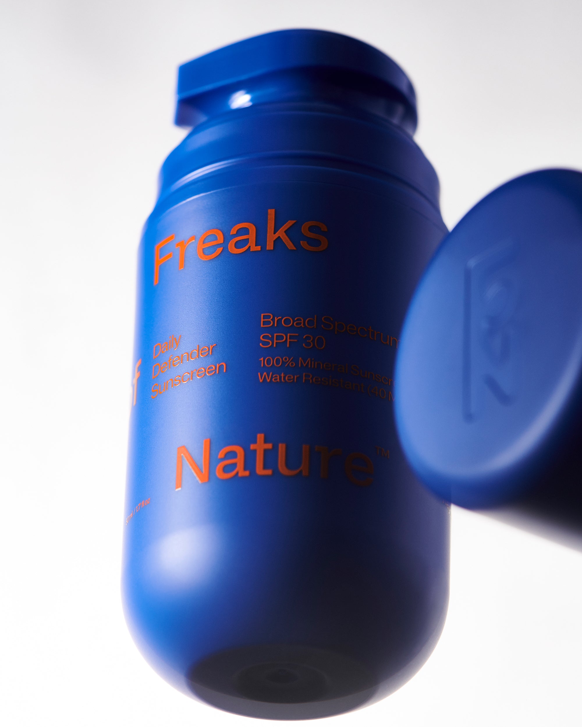 A close-up of a blue cylindrical SPF30 sunscreen bottle featuring "Freaks of Nature Skincare," "Daily System Sunscreen," "Broad Spectrum SPF 30," "100% Mineral Sunscreen," and "Water Resistant (40 min)." Infused with vegan Squalane, the bottle boasts a matching blue cap.