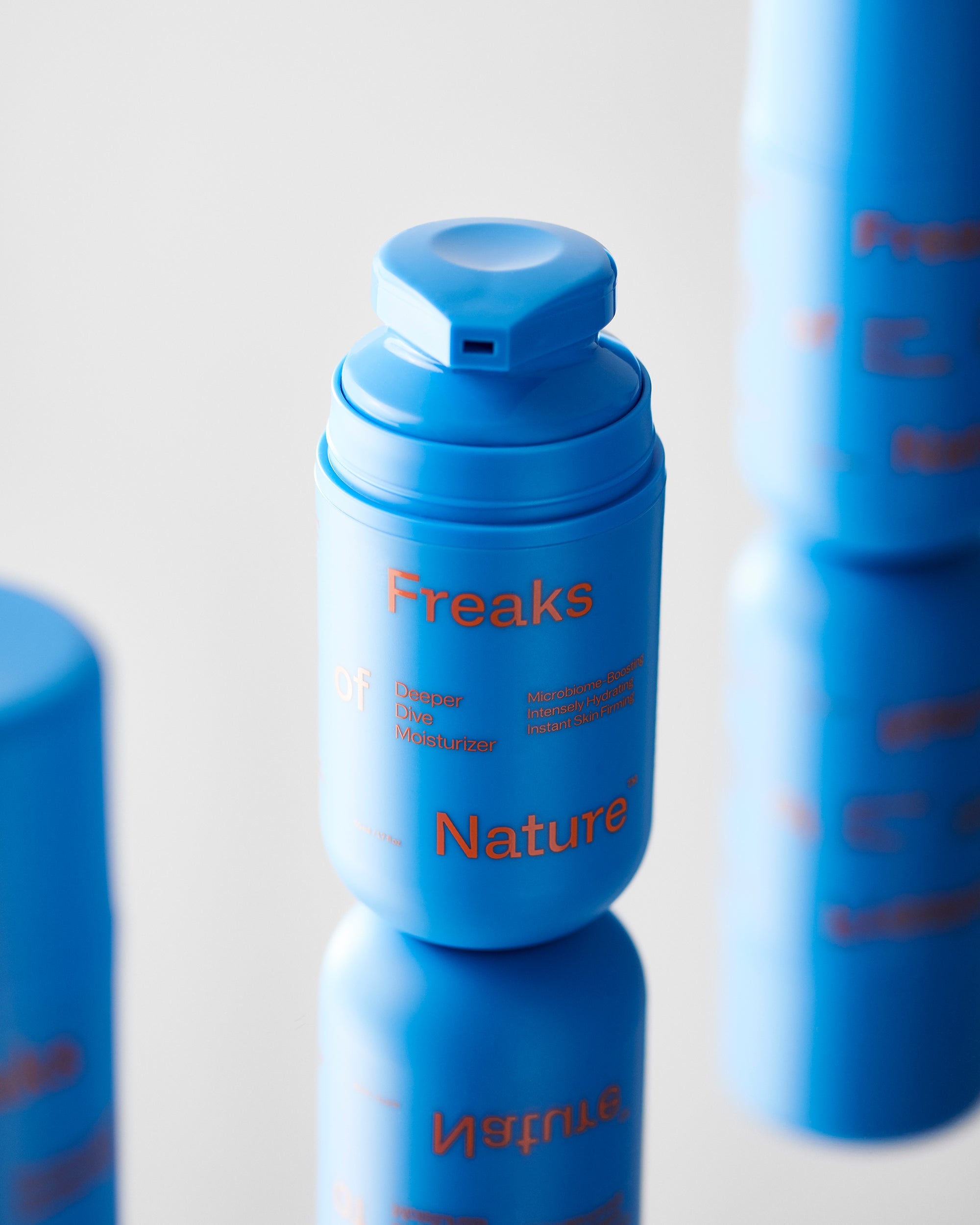 Close-up of a blue cylindrical bottle with a flip-top cap, labeled "Freaks of Nature Skincare" in orange text. The product appears to be an Endurance System, as indicated by the additional text on the bottle. The image has a reflective surface below.