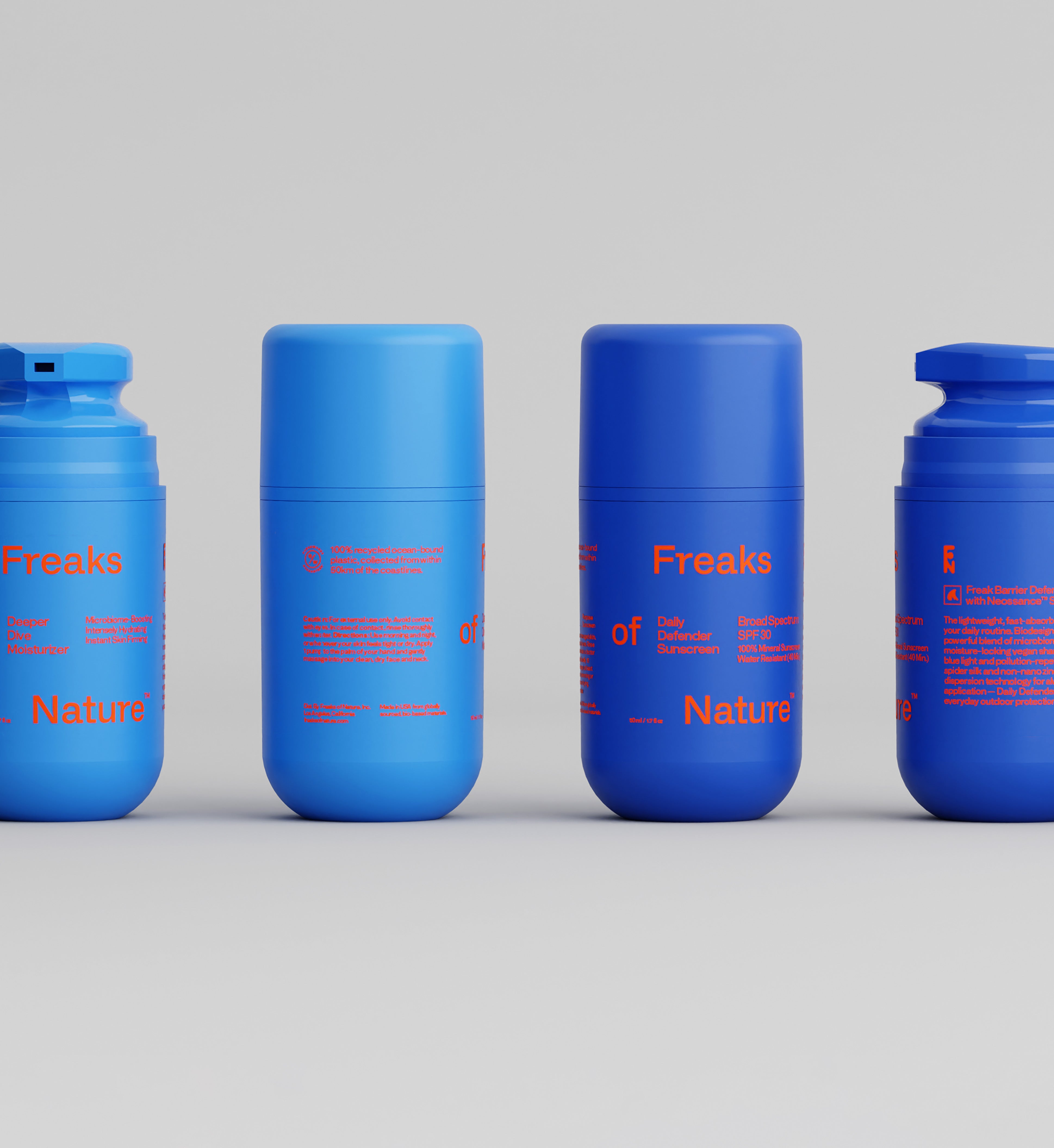 Four blue containers with "Freaks of Nature Skincare" printed on them in red text are displayed against a plain background. The containers, featuring Daily System with SPF30 Sunscreen and Deeper Dive Moisturizer Serum Gel with vegan Squalane, vary in lid styles, including flip-top and twist-on/off lids, and are arranged in a row. Additional text appears in smaller red font.