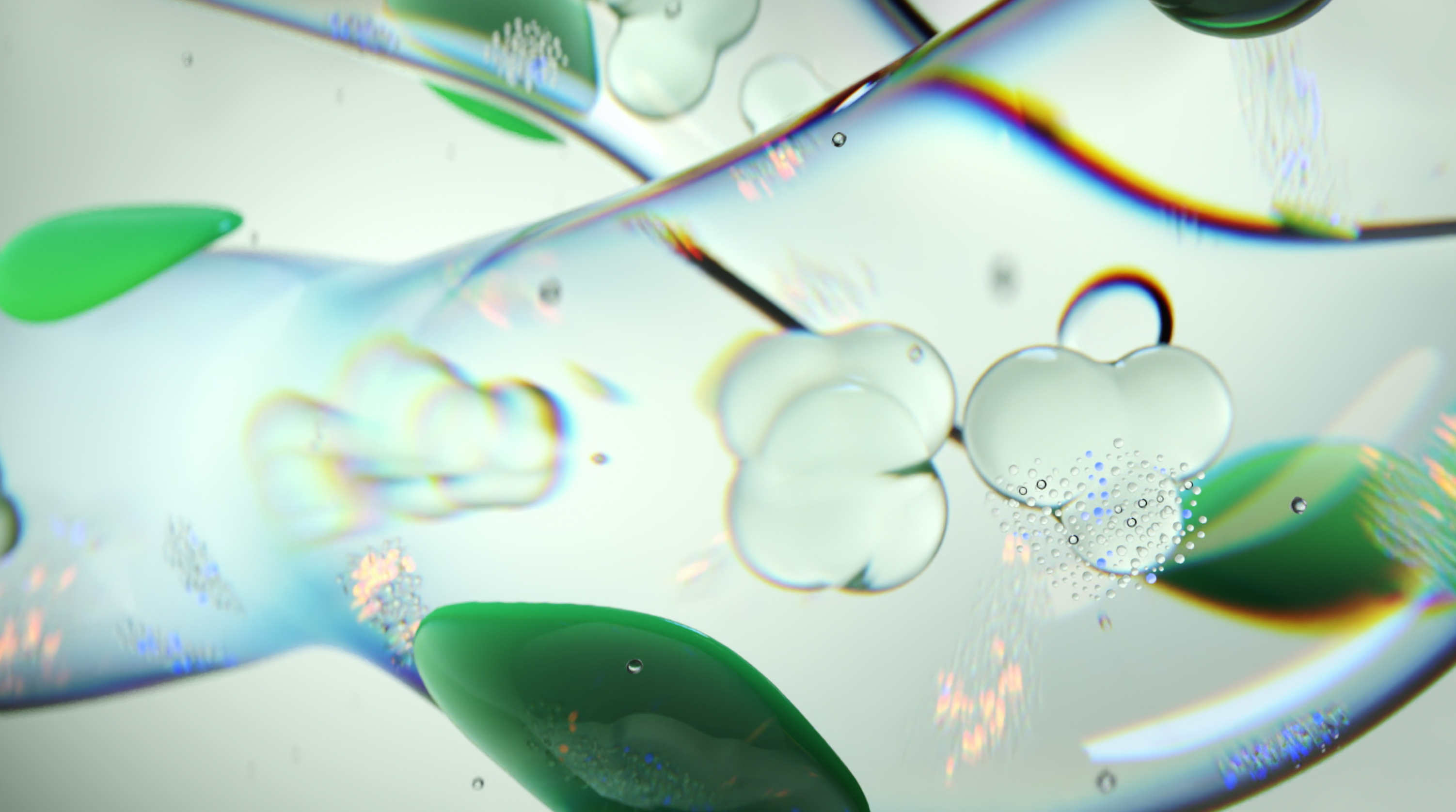 A close-up of a transparent gel-like substance with suspended green and clear droplets. The surface reflects light with a prism-like effect, creating a visually dynamic image. Small bubbles are also visible within the gel. The background is blurred.