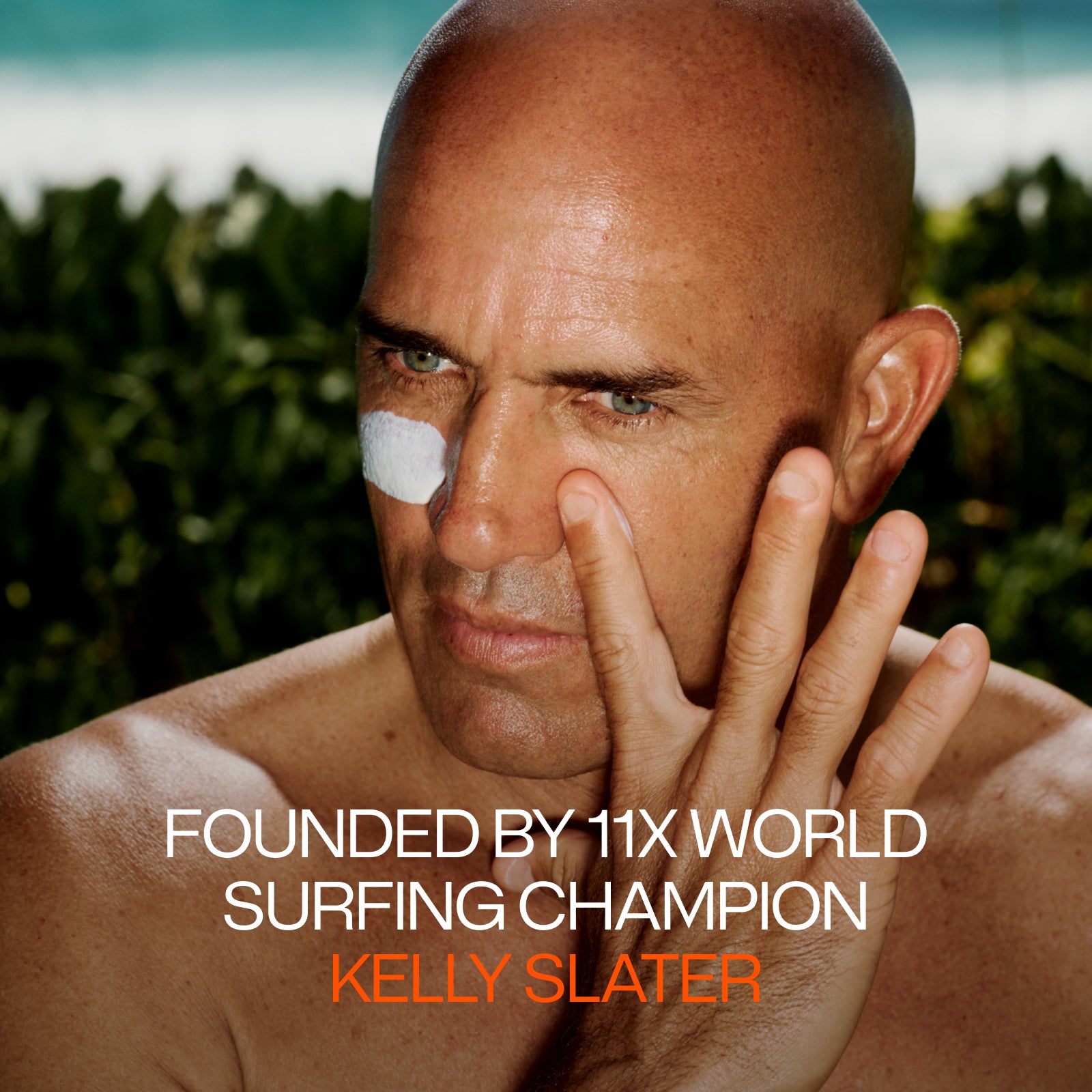 A bald man with tanned skin applies Endurance System from Freaks of Nature Skincare, enriched with SPF50 and microbiome-balancing properties, to his face while looking into the distance. The text reads: "Founded by 11x World Surfing Champion Kelly Slater." Lush greenery and the ocean are visible in the background.