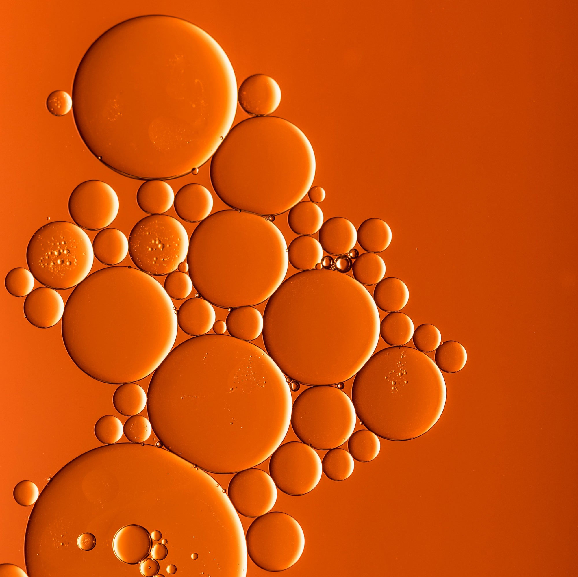 This image features an abstract composition of variously sized, circular bubbles clustered together on an orange background. The arrangement creates a visually intriguing geometric pattern, with some bubbles overlapping and others spaced apart.